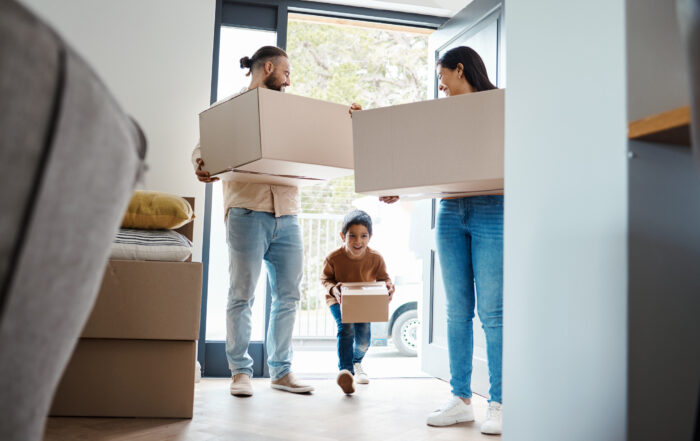 A smiling family carrying moving boxes into their new home. This happy moment reflects the security and peace of mind that Removalist Insurance can provide during a house move.