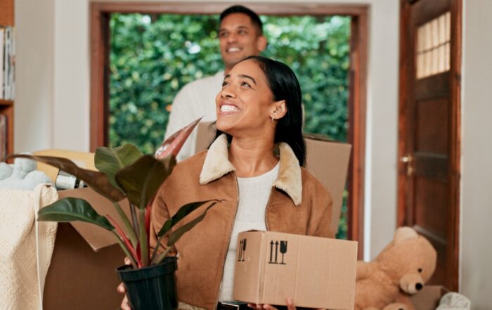 A woman walking into her new home with a box and smiling while family members follow behind, showing the confidence and reassurance that Removalist Insurance offers during the moving process.