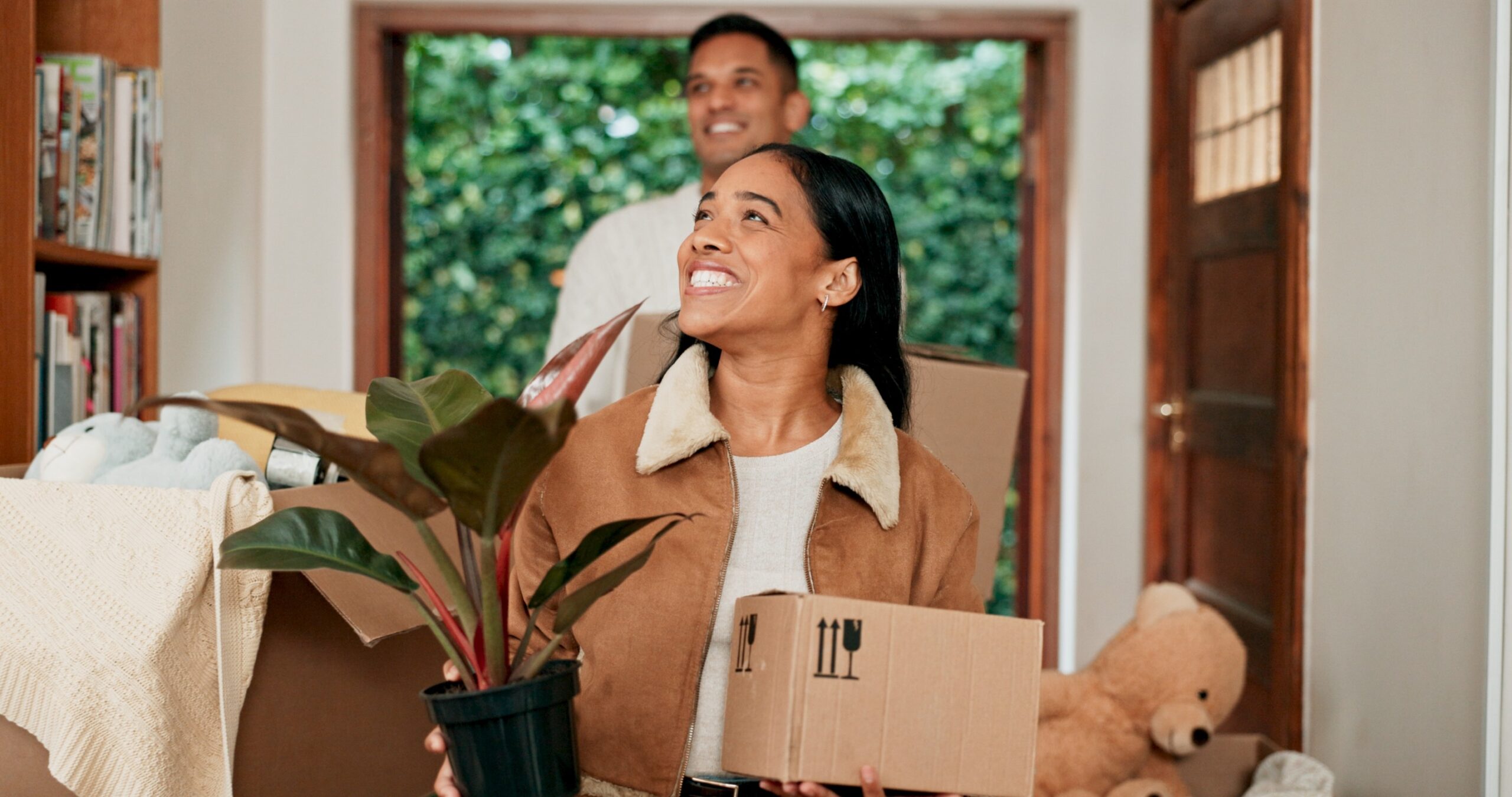 A woman walking into her new home with a box and smiling while family members follow behind, showing the confidence and reassurance that Removalist Insurance offers during the moving process.